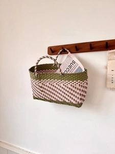 Detail of army green and pink woven basket bag hanging on a minimalist wood hook