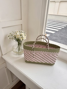 Close-up of woven handbag with olive green and pink checkerboard pattern on windowsill