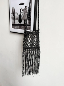 Macro shot of bohemian black macramé woven bag featuring long tassels on a white wall