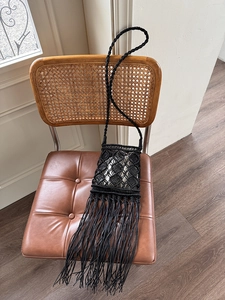 Detail of hand-woven black macrame crossbody bag with long fringes on vintage chair
