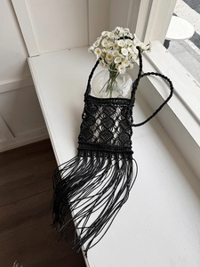 Detail of black macramé hand-woven bohemian crossbody bag with long tassels on a windowsill