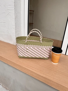Detail of handwoven picnic basket bag in pink and green on a sunlit wooden windowsill
