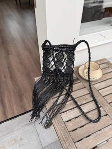 Detailed close-up of bohemian black macrame crossbody bag with long tassels on wooden table