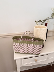 Detail of olive green and pink hand-woven shopping basket on a white vintage wooden cabinet