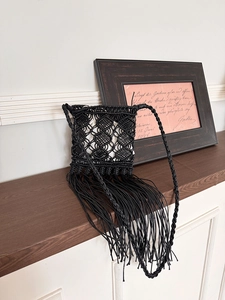 Detail of a handmade black macrame crossbody bag with long fringes on a wooden shelf