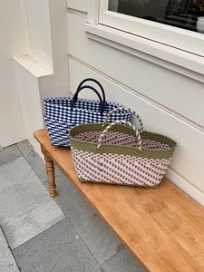 Detail of hand-woven basket bags in blue-white and green-pink patterns on a wooden bench