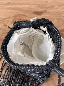 Detail of black handwoven bucket bag with beige drawstring closure and fringe accents