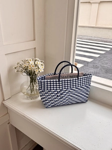 Detail view of a blue and white checkered hand-woven tote bag with dual black handles