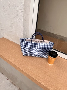Detail view of a blue and white checkered woven tote bag on a rustic wooden terrace