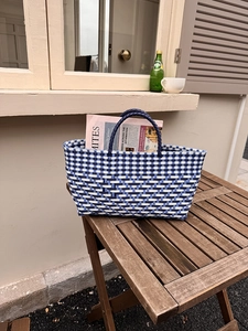 Close-up of blue and white woven checkered handbag on a wooden table with outdoor setting