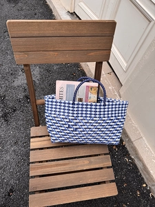 Detailed blue and white checkered woven tote bag with durable handles on a wooden chair