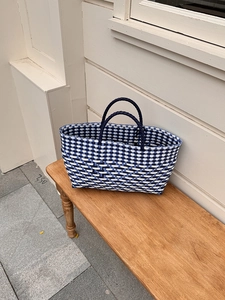Detail view of handmade woven tote bag with blue checkerboard pattern on a wooden bench