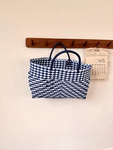 Detail of blue and white checkered hand-woven tote bag hanging on a wooden hook