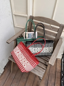 Detailed view of three woven beach tote bags in red, black, and green on a wooden bench
