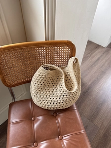 Détail d'un sac cabas en paille beige avec crochet délicat posé sur une chaise rétro