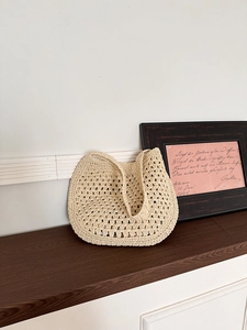 Détail du sac cabas en paille beige avec tissage au crochet ajouré sur surface en bois