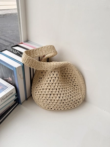 Détail du sac cabas beige tissé ajouré posé sur des livres avec un éclairage doux
