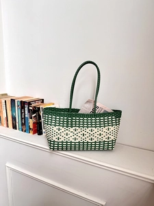 Detail view of a green and white checkered woven tote bag with slim round handles