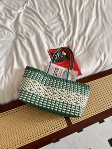 Detailed close-up of green and white woven tote bag with straw texture on a rattan stand