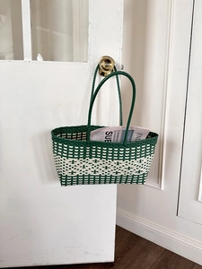 Detail of woven beach tote bag with green and beige geometric pattern hanging on a white door