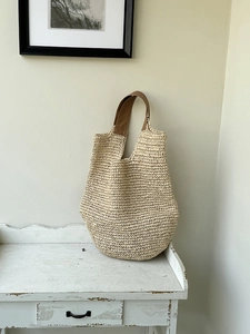 Handwoven straw tote bag with brown leather handles placed on a vintage white cabinet