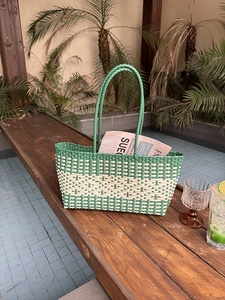Detail of green and beige striped woven tote bag featuring round handles and beach style