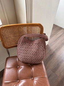 Détail du sac hobo au crochet rose poudré avec large bandoulière tressée sur une chaise