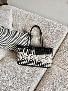 Detail of black and white checkered woven tote bag on a soft white boucle sofa