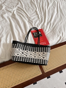 Detail of hand-woven tote bag with black and white grid pattern on a wooden bench