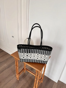 Close-up of black and white woven tote bag with dual handles on a wooden table