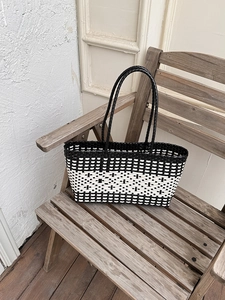 Detail of black and white woven tote bag on a wooden bench with intricate braided texture