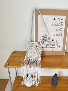 White macrame tassel crossbody bag with bohemian woven pattern on a wooden shelf