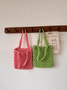 Detail of pink and green hand-woven cotton rope mesh tote bags on a wooden wall hanger