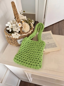 Close-up of bright green hand-woven net handbag on a white wooden surface