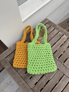 Detail of handmade hollow net woven handbag with textured knit patterns in green and yellow