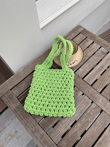 Detailed view of neon green handmade woven mesh bag on a rustic wood table