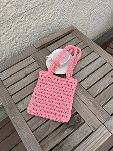 Close-up of pink handmade woven beach bag showing detailed crochet knit texture on wood