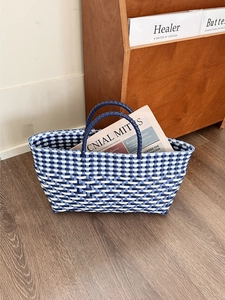 Handwoven blue and white checkered tote bag with double handles on dark wood floor