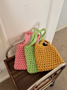 Close-up of pink green and yellow handwoven crochet hollow net beach tote bags