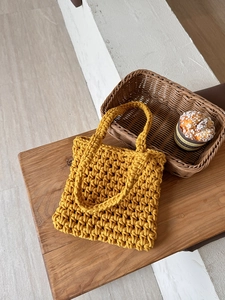 Detail of ginger yellow hand-woven hollow fishnet bag texture on a wooden bench