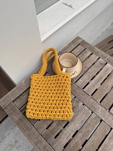 Detail of yellow handmade hollow mesh woven bag on a wooden table with coffee cup