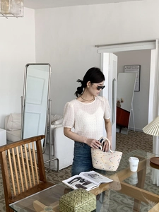 Detail of a white textured puff sleeve top paired with a woven bag in a chic home setting