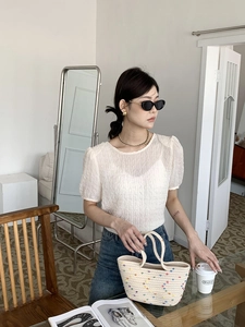 Detailed close-up of cream textured short-sleeve top with chic woven cotton handbag