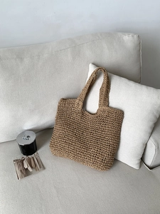 Detail of handwoven straw tote bag with tight cross-weave texture on a neutral sofa
