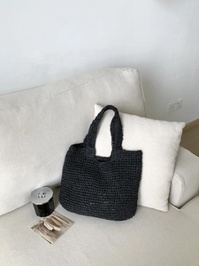 Detail of black woven straw tote bag featuring intricate texture and minimalist handles