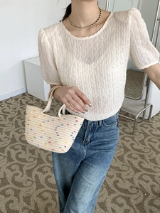 Detail of a beige woven handbag with colorful polka dots paired with a white textured top