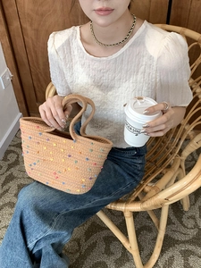Close-up of woven cotton tote bag with colorful pom poms held by a model