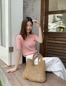 Detail of a large woven straw beach bag paired with a pink polo shirt and white pants
