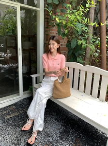Close-up of a brown woven straw tote bag paired with casual vacation style outfit