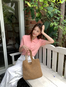 Detail of a brown openwork woven straw bag held with a pink knitted polo shirt